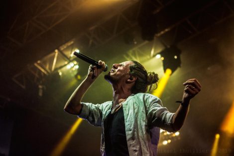 Der Reggae-Musiker Naâman singt voller Energie in sein Mikrofon. Im Hintergrund die Bühnenbeleuchtung.
