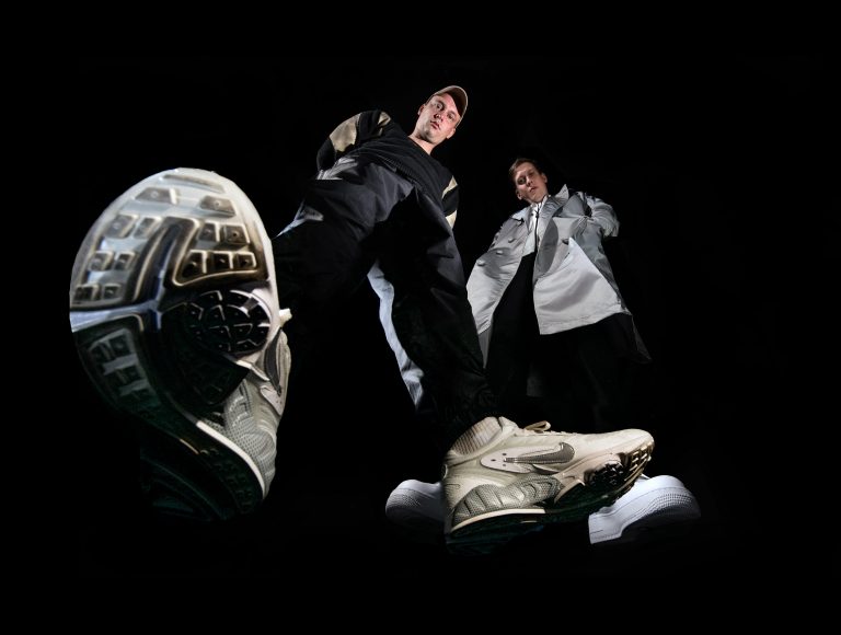Froschperspektive von Grim104 und Testo vor schwarzem Hintergrund (Hip Hop Duo Zugezogen Maskulin)
