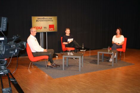 Peter Stein, Moderator Alex und Katrin Zschau sitzen im Halbkreis Richtung Kameras. Im Hintergrund steht ein Monitor mit der Aufschrift "SpeedDate zur Wahl: CDU vs SPD"