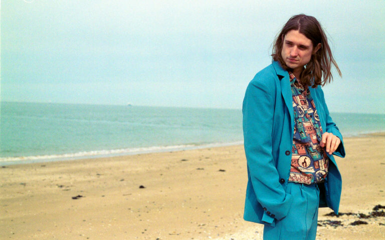 Dominic Gore in blauem Anzug am Strand vor Küstenstreifen