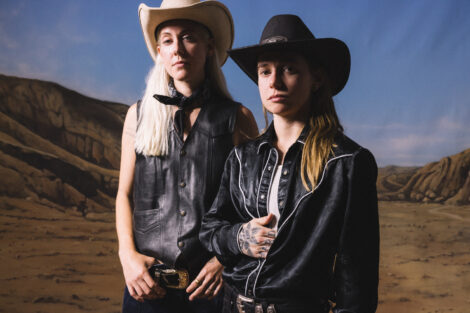 Julien Baker & TORRES tragen Cowboyhüte und stehen vor einer gemalten Landschaft